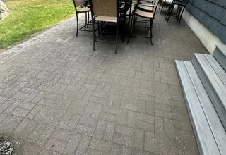 Backyard paver patio with dining set beside a gray composite deck and shingle siding